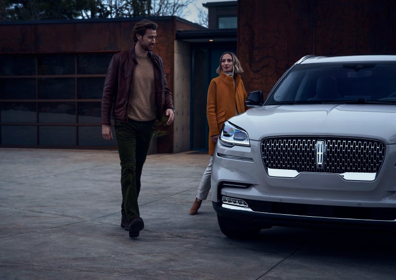 A man and a woman approaching a 2024 Lincoln Aviator® SUV, which illuminates certain lights when they are close | Irwin Lincoln Laconia in Laconia NH